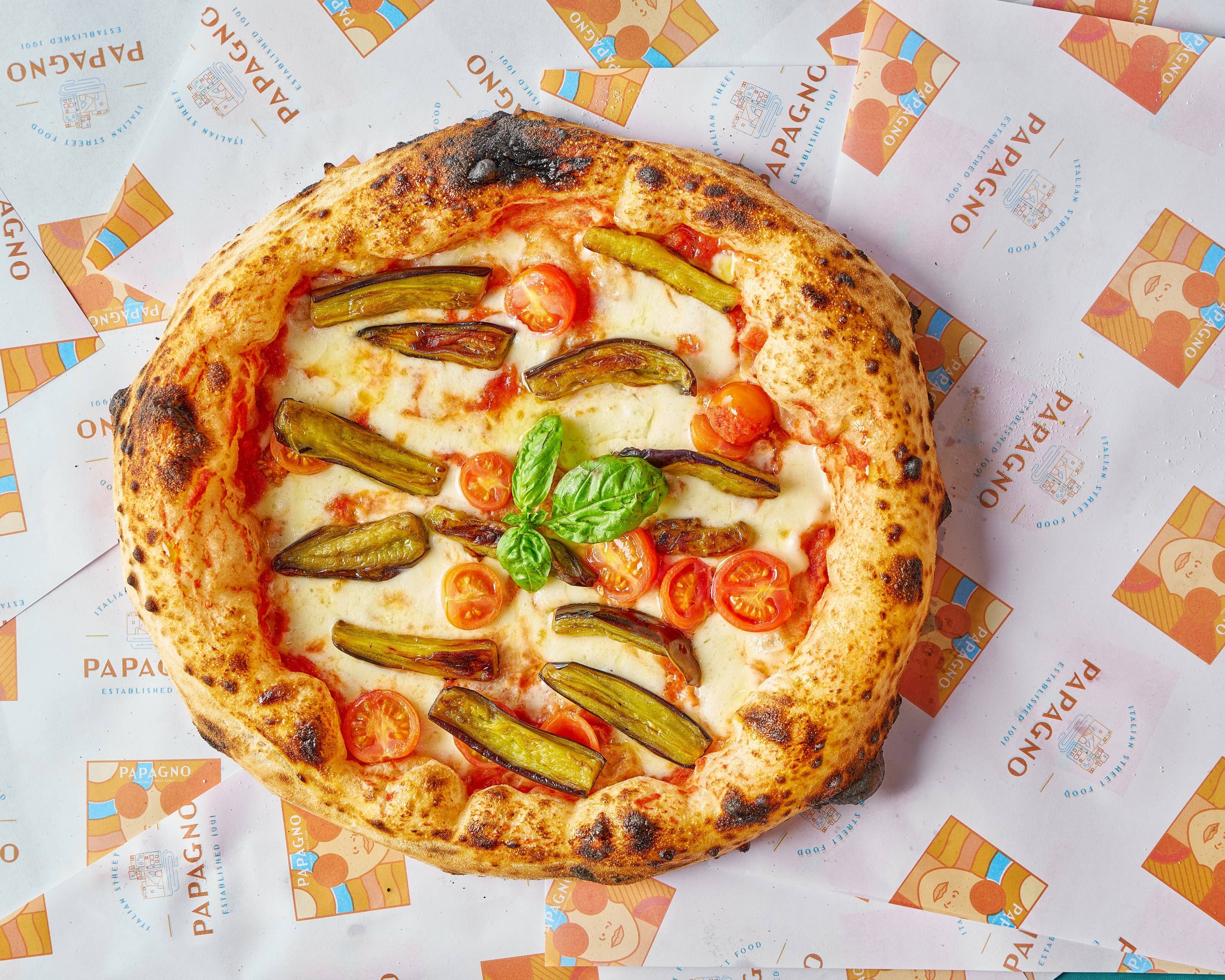Pizza vue de dessus garnie de lamelles d'aubergine, de tomates cerises et de basilic, cornicione régulier.