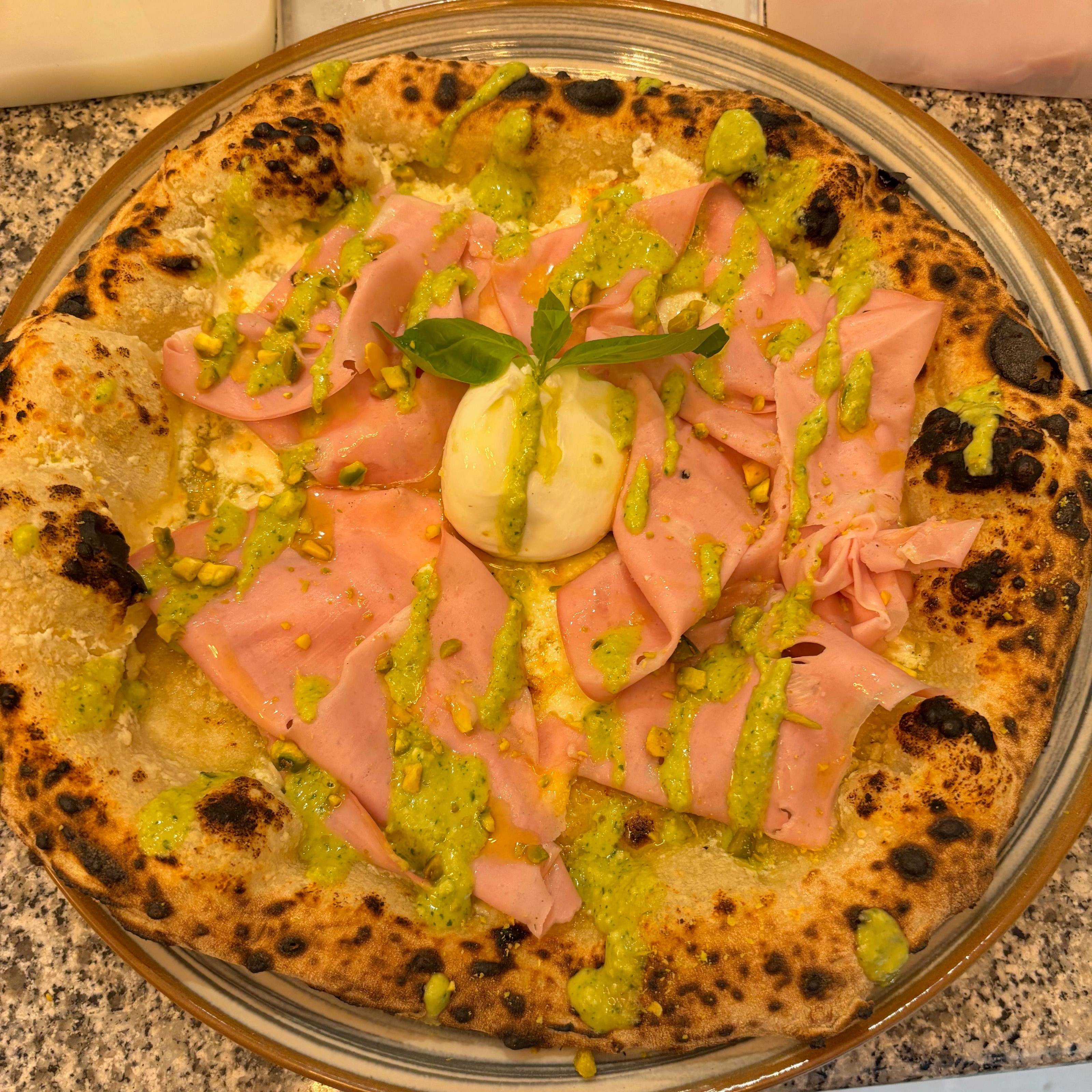 Pizza blanche vue de dessus, couverte de mortadelle, d'une burrata au centre et de pesto de pistache.