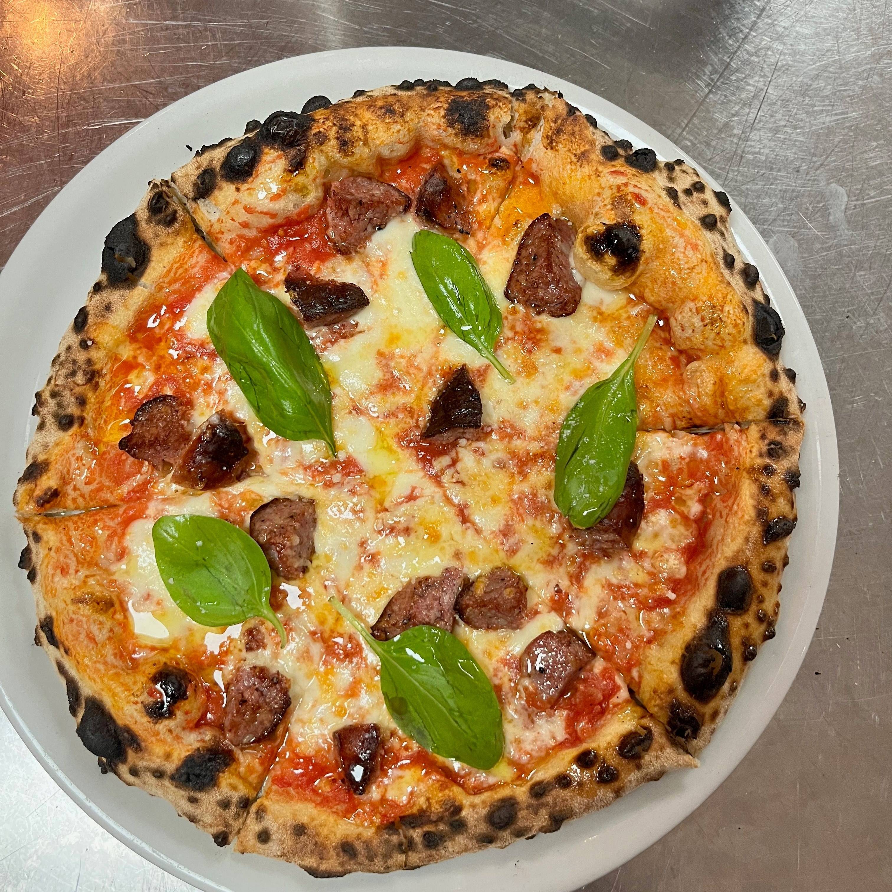 Pizza vue de dessus garnie de morceaux de saucisse, de mozzarella et de feuilles de basilic.